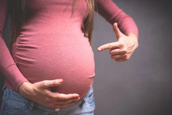 Hamile bir kadın gri bir arka planda el ele tutuşuyor. Kopyalama alanı, hamilelik, annelik, insanlar ve beklenti konsepti. Yakın plan, fotokopi odası, kapalı alan. Hamileliğin tonlu fotoğrafı. — Stok fotoğraf