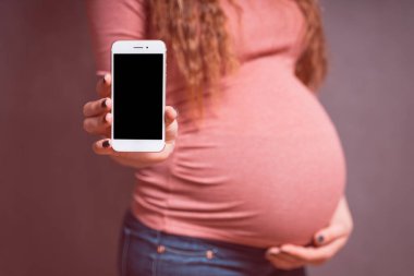Akıllı telefonlu hamile bir kadın, cep telefonunu boş ekranla gösteriyor. Akıllı telefon modeli, mobil uygulamalar için kopyalama alanı. Hamilelik, Teknoloji, hazırlık ve beklenti konsepti.