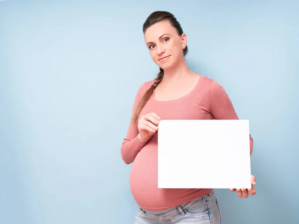 Junge schöne schwangere Frau vor isoliertem blauen Hintergrund mit einem leeren Blatt Papier. Lifestyle-Konzept, Ihren Text hier. Kopierraum — Stockfoto