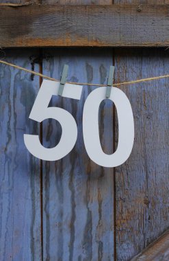 Sayı 50 kağıttan kesilmiş ve rustik bir boyalı mavi ahır kapısı önünde dize üzerine saptanmış. Ellinci Doğum günü veya yıldönümü kutlama kiraz kuşu 
