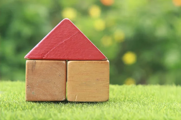 House from Wooden Block Toy at Fresh Green Grass with blur Tree and Yellow Flower