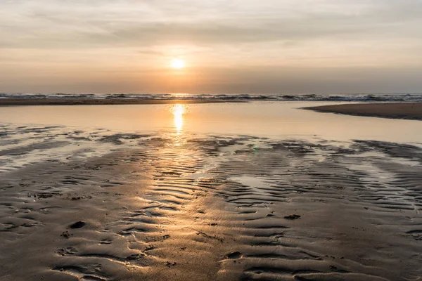 Kuzey Denizi beach Egmond aan Zee, Hollanda gümüş günbatımında. Batan güneşin su birikintileri ve ıslak sahil kumu ribbles yansıtır