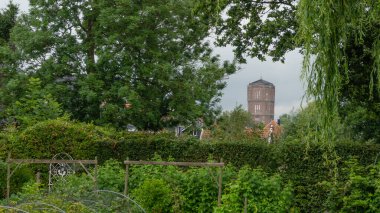 Kwadijk 'in tuğladan yapılmış su kulesinin çerçeveli görüntüsü, arka bahçenin yemyeşil bahçesinden bakıyor. Korunan anıt ve simge. Kwadijk, Kuzey Hollanda, Hollanda.