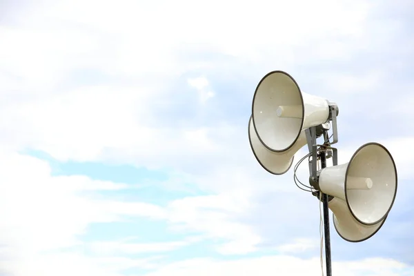 stand of multiple loud speakers against a plain cloudy sky background. Concept for deafness, hearing, news, alarm, warning, announcements and speakers.