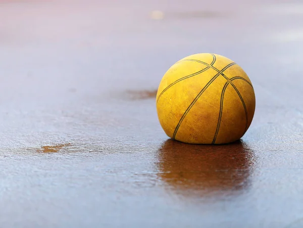 A flat deflated old tired yellow basket ball on wet concrete ground. Concept for feeling flat, bad poor rainy weather, tired, sick or need help.