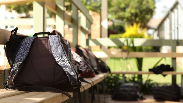 composition of school bags back packs duffle bags outside a classroom at a secondary high school on outside bench seats chairs. Education setting without students. School yard, classroom. Pedagogy, teaching, school student concept