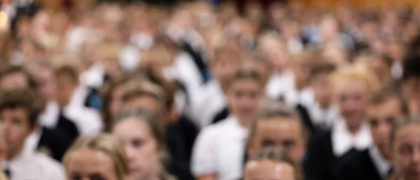 wide 3/4 view of highschool school students in uniform seated at assembly in uniform facing the front. Heavy blur, soft focus many faces crowd shot. Deliberate blur effect to avoid identity