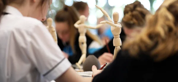 Visual Art high school students working from wooden mannequins practicing drawing human fugure and correct proportion. Artists being creative the art room. Creativity inspiration concept