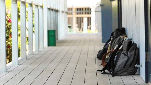 A number of school bags outside a classroom at high school. Long narrow hallway or outdoor corridor with bright sunshine. Educational theme or concept. Backpacks in the school yard. Back to school, bullying, anxiety, pressure.