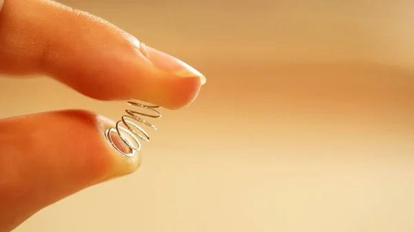 extreme close up of fingers depressing, pushing a tiny chrome spring down. Silly, scared to exercise concept. Idea for weight loss, exercise program and gym junkie theme.