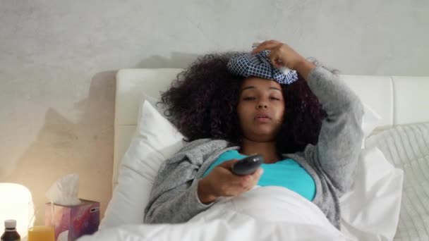 Больная афроамериканка с лихорадкой, смотрящая фильм по телевизору — стоковое видео