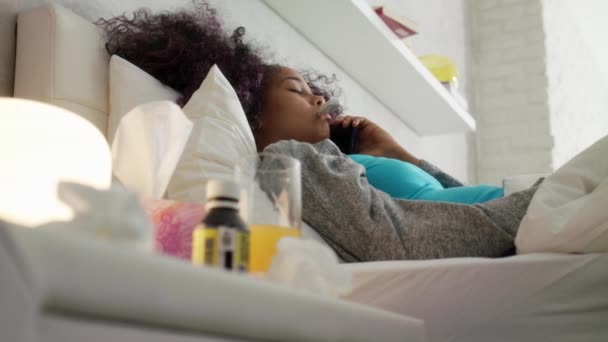 Chica con fiebre usando termómetro llama al médico por teléfono — Vídeo de stock