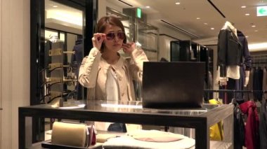 Asya insanlar moda ürünler ve aksesuarlar için alışveriş. Japon kadın lüks mağaza alışveriş merkezi içinde. Bayan mağaza yeni güneş gözlüğü satın alma ve yardım ve destek dostu satış asistanı konuşuyor
