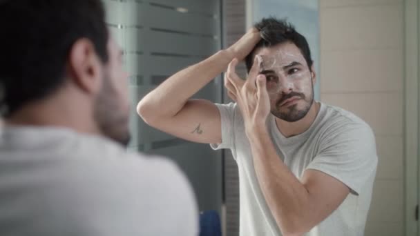Молодой человек наносит антивозрастной крем на лицо для ухода за кожей — стоковое видео