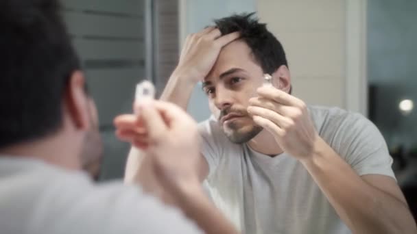 Молодой человек применяет лосьон для лечения алопеции и выпадения волос — стоковое видео