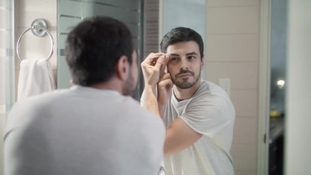 Homem latino aparando a sobrancelha para o cuidado do corpo no banheiro — Vídeo de Stock