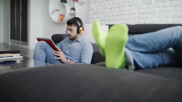 Paar liegt mit Tablet-PC und Kopfhörer auf Sofa — Stockvideo