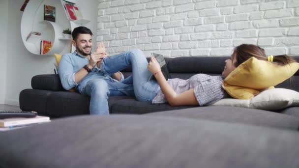 Мужчина массирует ноги подруги на диване дома — стоковое видео