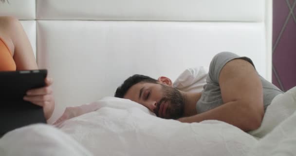 Mujer trabajando en la cama en casa y hombre durmiendo — Vídeo de stock