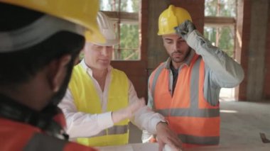 İnşaat alanında çalışan insanlar. Erkekler yeni evin içinde apartman içinde işte. Takım mühendis ile konuşmak ve planı iş toplantı sırasında seyir işyerinde işçilerin