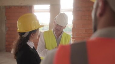 İnşaat alanında çalışan insanlar. Erkek ve kadın yeni evin içinde apartman içinde işte. Danışman ve işçi ile konuşmak ve proje planları iş toplantı sırasında arayan patron