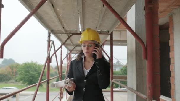在建筑工地工作的人 妇女在工作作为建筑师在新的房子在公寓大厦之内 工程师走在脚手架上 用手机说话 — 图库视频影像