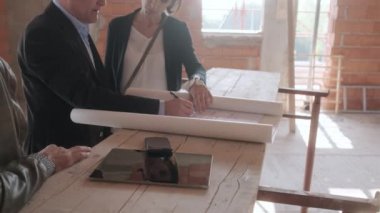 Yeni binada müşterilerle konuşurken satış acentası. Emlak İnşaat alanı olarak müşteriler ile çalışan adam. Emlak broker gösteren ev karı koca için. Yeni ev alıcılar olarak genç çift