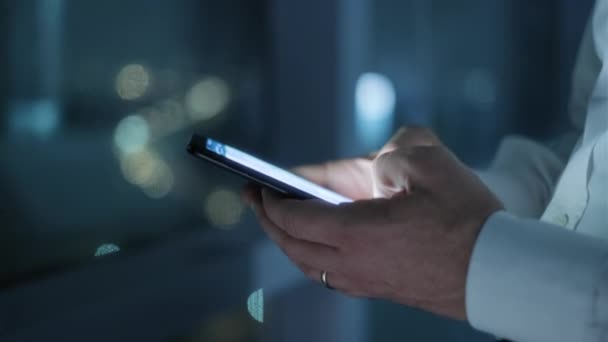 深夜在现代办公室工作的人 工作场所的白人商人 忙碌的高加索经理在工作与手机 背景中的城市灯光 手持智能手机的手特写 — 图库视频影像