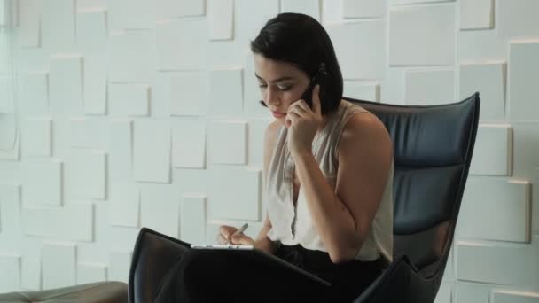 ビジネスの女性の携帯電話とタブレット コンピューターとオフィス 忙しいラテン系事務作業といえば携帯電話で動作します 笑みを浮かべて 待合室でヒスパニック系のマネージャーとしてワーカー実業家 — ストック動画