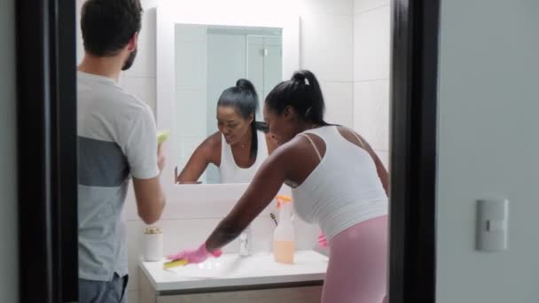 跨种族夫妇在家里做家务活和打扫浴室 非裔美国人妻子帮助白人丈夫在厕所里用肥皂 洗涤剂和清洁剂 与幸福的已婚人士一起做家务 — 图库视频影像