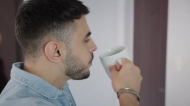 Coronavirüs salgınına karşı korunmak için N95 maskesi takan bir kadın kahve içen ve sabah kahvaltısını evde yapan bir adamı öpüyor. İnsanlar ve Covid-19 salgını