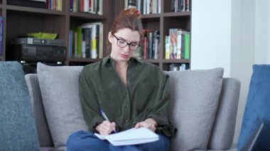 Üniversite öğrencisi olan ve ders çalışan bir kadın. Kız üniversite eğitimi sınavına hazırlanıyor, akıllı telefondan gelen mesajlara bakıyor. İnternet ve sosyal medya için cep telefonu olan gençler kanepede