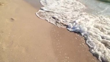 Genç kadın bacakları beyaz kumda yürüyor. Adanın sahilinde dalgalar var. Sinematik.