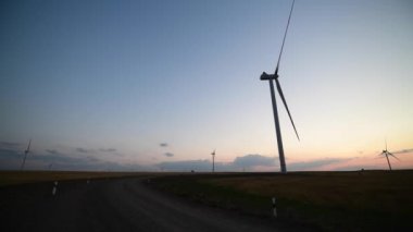 Yel değirmeni çiftliğinin manzarası, günbatımında enerji üretimi için rüzgar jeneratörleri. Rüzgar güç türbinleri temiz yenilenebilir enerji üretiyor