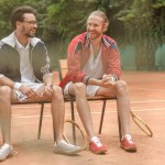 Amigos deportivos felices con raquetas de madera sentados en sillas en la cancha de tenis