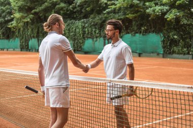 athletic tennis players with wooden rackets shaking hands after match on court clipart