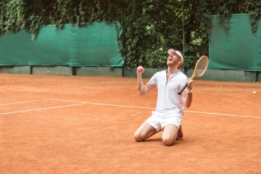 kutluyor ve tenis kortunda diz çökmüş raket ile sarışın kazanan