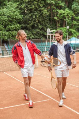 Ahşap raketler tenis kortunda yürüyüş ile gülümseyen arkadaşlar