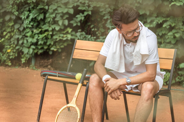 усталый теннисист с полотенцем и теннисной ракеткой, отдыхающий на стуле на теннисном корте
 