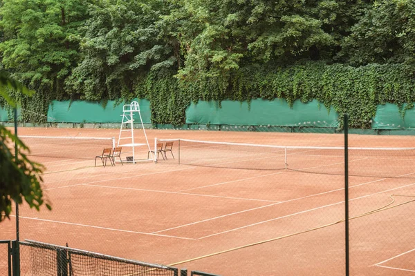 Utsikt Över Brun Tennisbana Med Net Stolar Och Träd — Gratis stockfoto