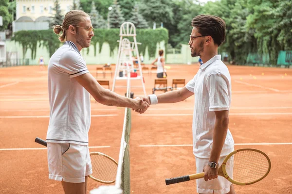 Old-fashioned tennis players with wooden rackets shaking hands after game on court — Stock Photo