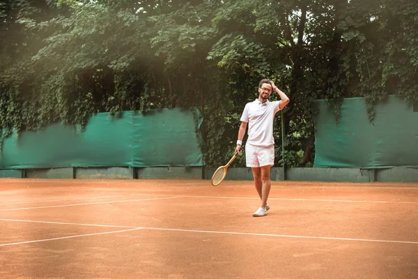 Jugador de tenis guapo con raqueta de pie en la pista de tenis - foto de stock