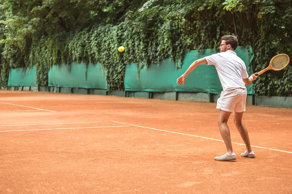 Sportif à l'ancienne jouant au tennis avec raquette et balle sur un court de tennis — Photo de stock