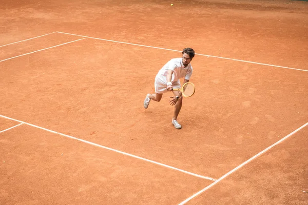 Handsome tennis player training with wooden racket on brown court — Stock Photo