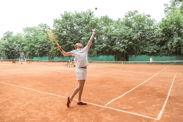 Guapo tenista con raqueta lanzando pelota en pista de tenis - foto de stock