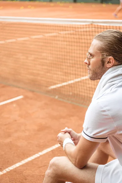 Old-fashioned tennis player with towel resting on brown tennis court with net — Stock Photo