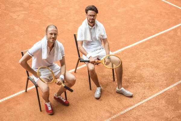 Tennis players with vintage wooden rackets resting on chairs — Stock Photo