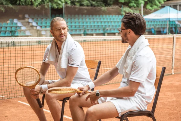 Handsome athletic tennis players with retro wooden rackets resting on chairs — Stock Photo