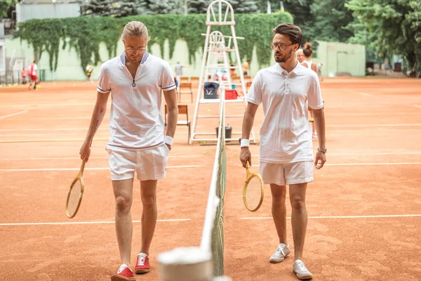 Tennis players with wooden rackets walking near net on court — Stock Photo