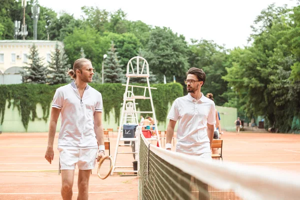 Jugadores de tenis con raquetas de madera caminando cerca de la red en la cancha - foto de stock